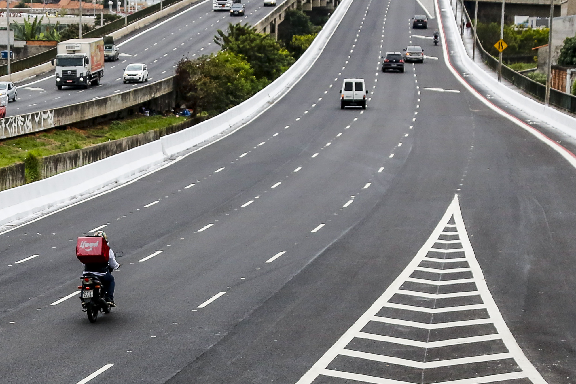 #PraTodosVerem visualiza-se a imagem de quatro carros, vistos de trás, passando por uma avenida.